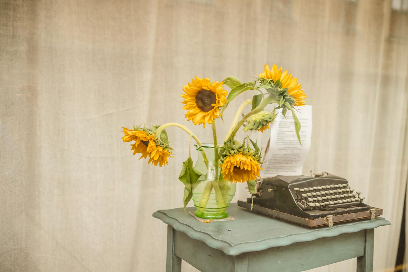 A classic typewriter with a vibrant sunflower arrangement on a wooden table.